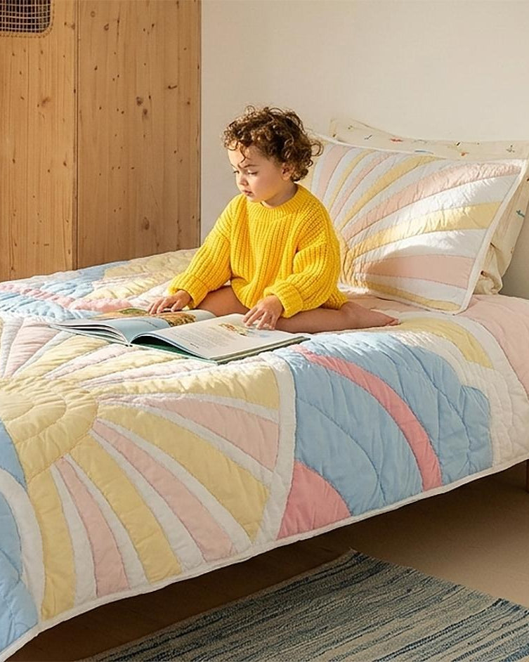 Child reading on a bed with the Sunrise Glow kids AC quilt