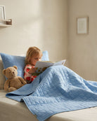 Child reading under the Blue Rainbow kids AC quilt